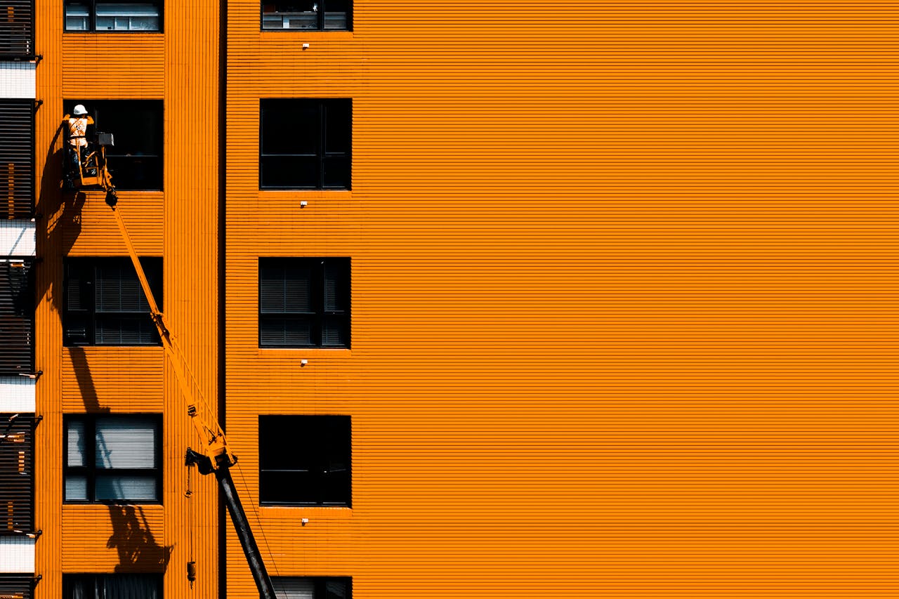 creative-03 A construction worker using a cherry picker working on an orange building facade.