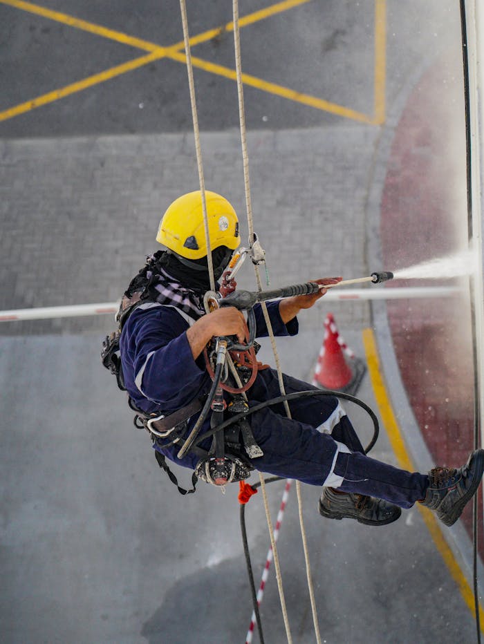 creative-03 A worker in safety gear high up cleaning a building with a pressure washer in Dubai.