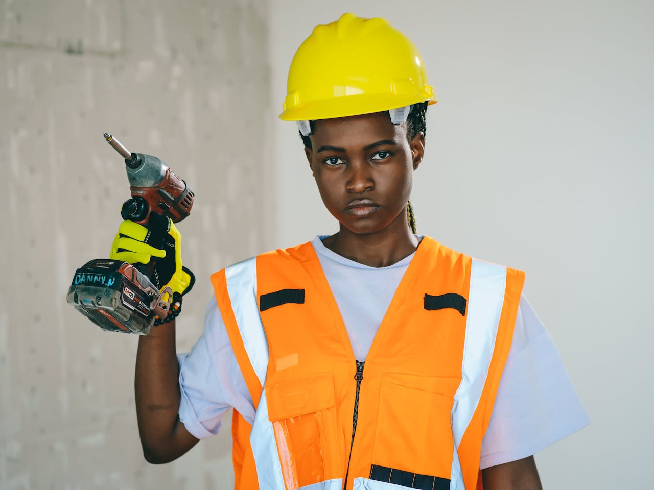 brand-01 A determined construction worker holding a drill in safety gear indoors.