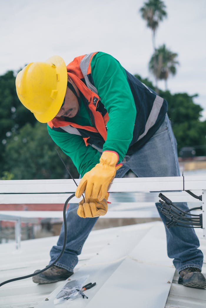creative-01 A construction worker wearing PPE installs electrical equipment on a roof.